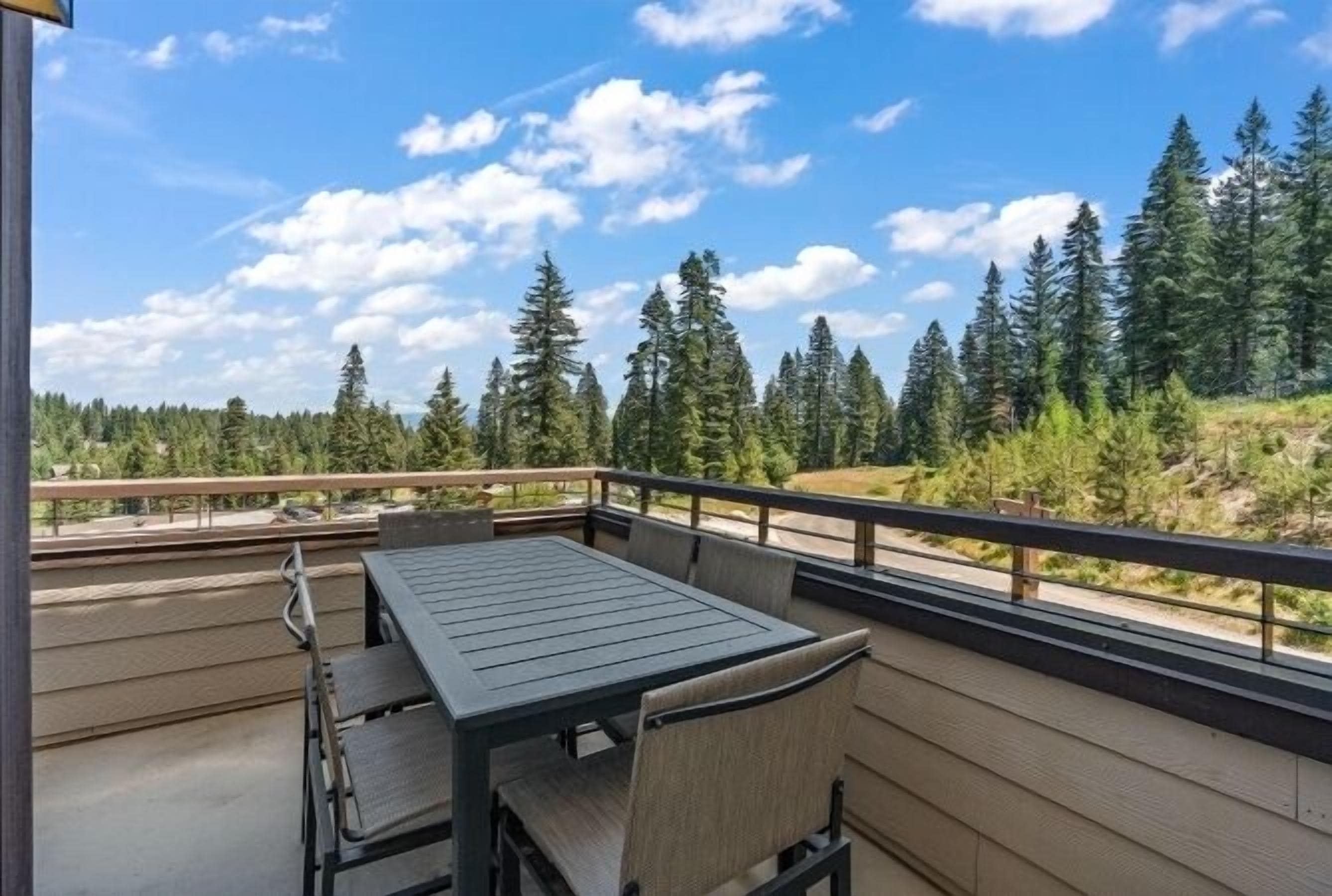 A balcony with a table and chairs, overlooking a forested area.