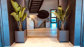 Un moderno vestíbulo de hotel con piso de mármol, una escalera y plantas en macetas grandes.