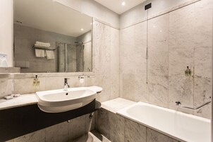 A modern bathroom with a large mirror, a sink, a bathtub, and a shower area.