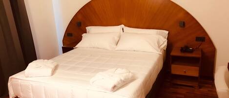A neatly made bed with white linens and two towels, a wooden headboard, a bedside table with a phone, and a wooden floor.