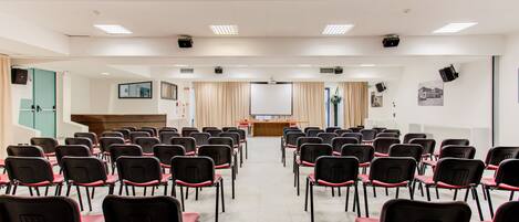 A conference room with rows of chairs, a podium, and a projector screen.