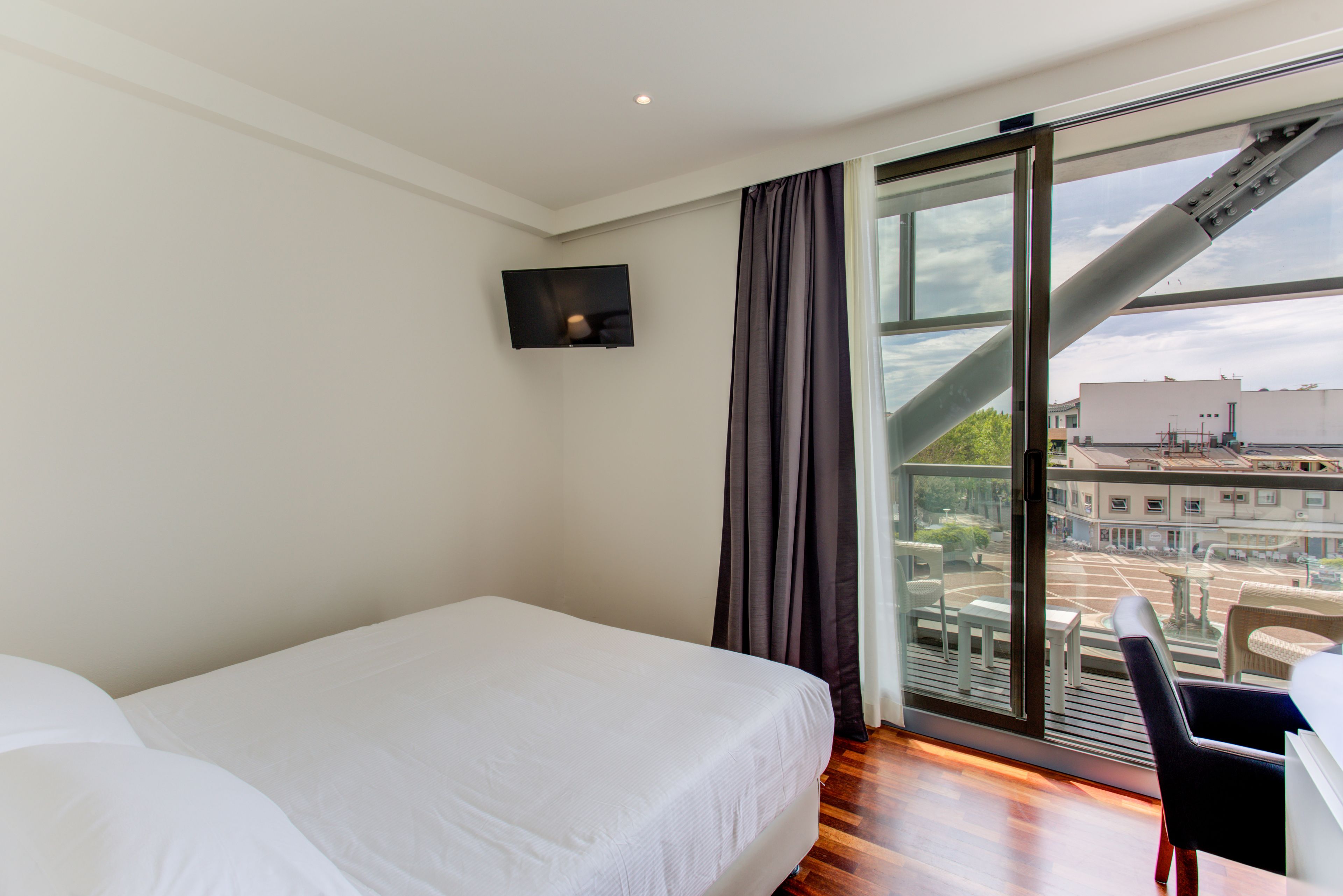 A hotel room with a bed, a desk, and a large window with a view of the city.