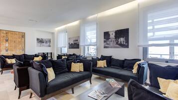 A modern hotel lobby with multiple black sofas, a coffee table, and large windows.