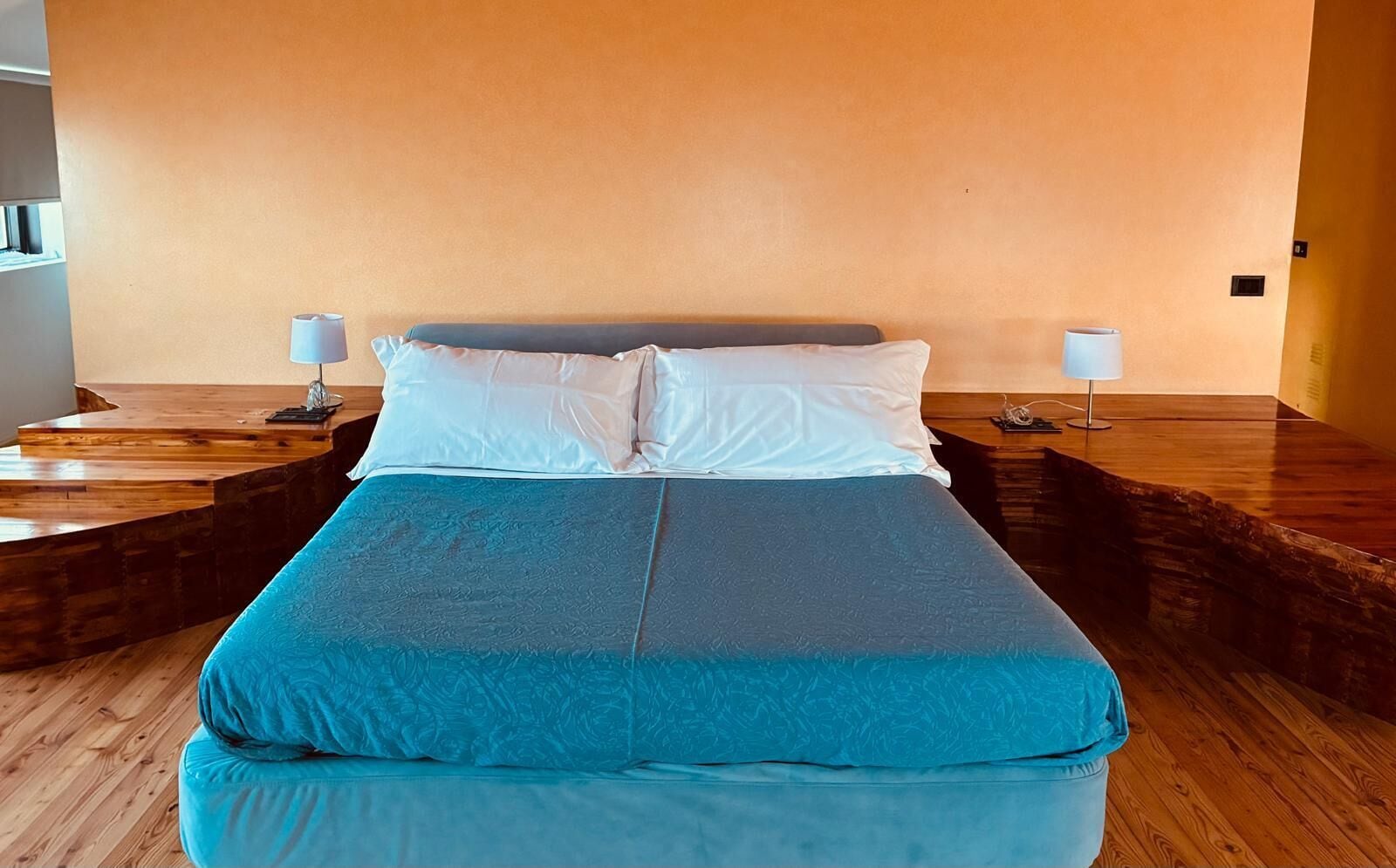 A bed with a blue and grey bedspread, two white pillows, and two bedside lamps.