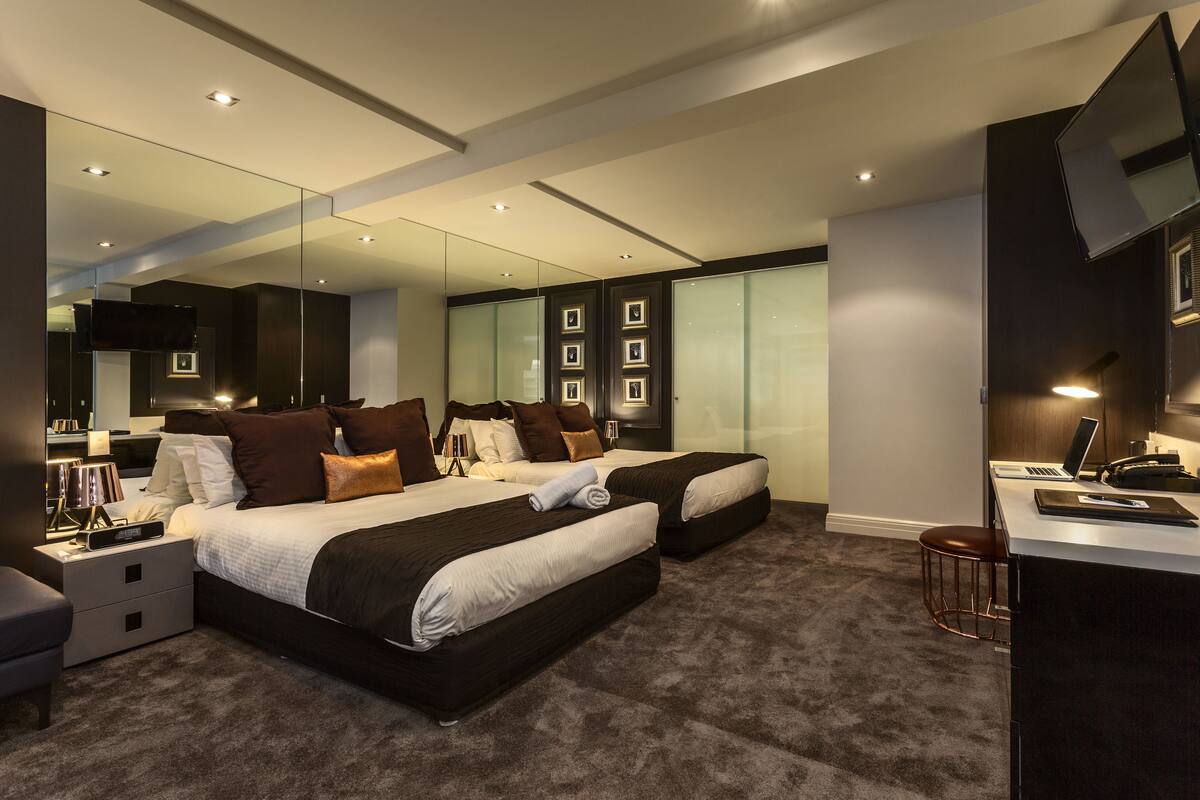Una habitación de hotel moderna con dos camas, un escritorio, una silla y un televisor.