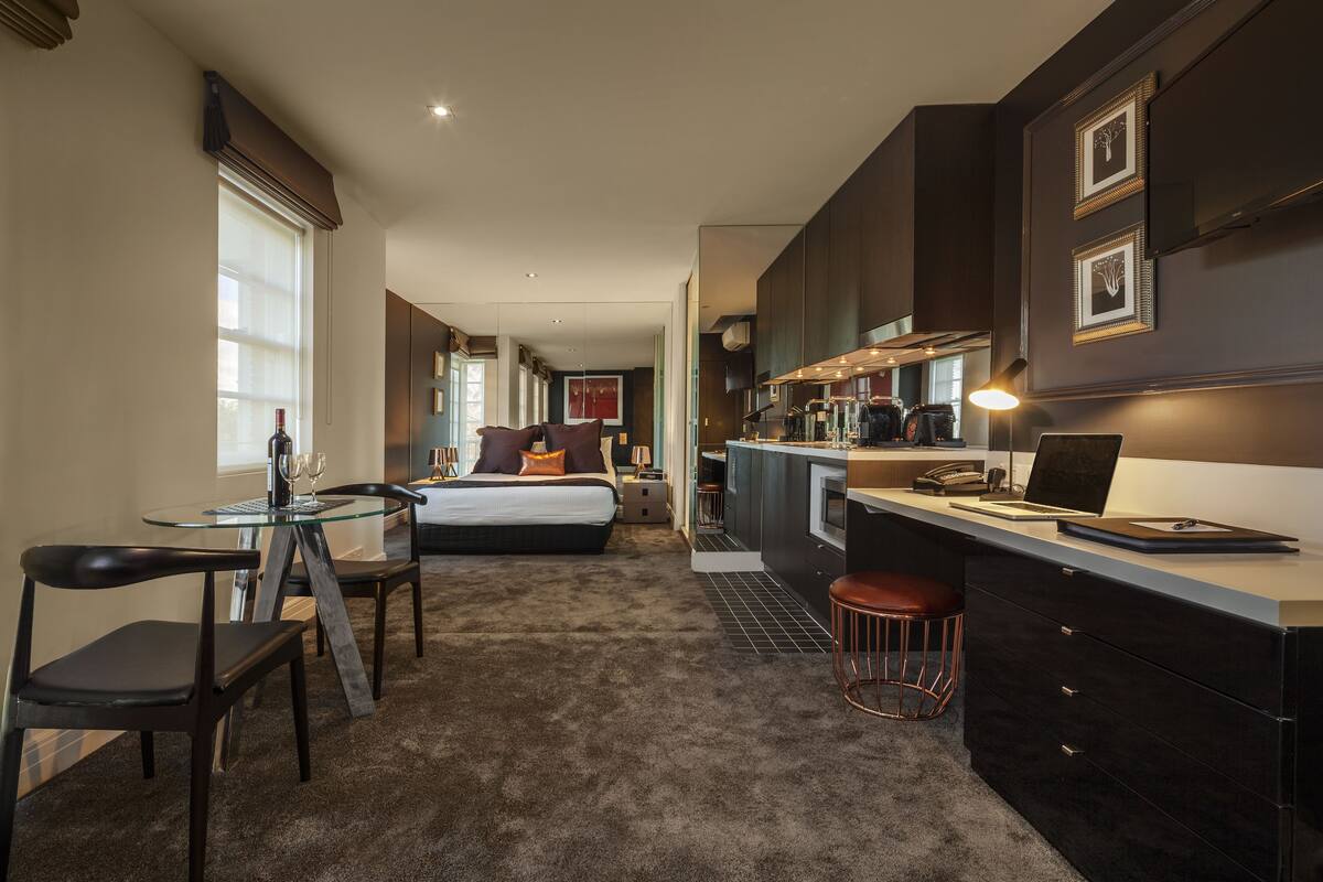 Una habitación de hotel moderna con zona de comedor separada, kitchenette y una cama grande.