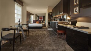 Una habitación de hotel moderna con zona de comedor separada, kitchenette y una cama grande.
