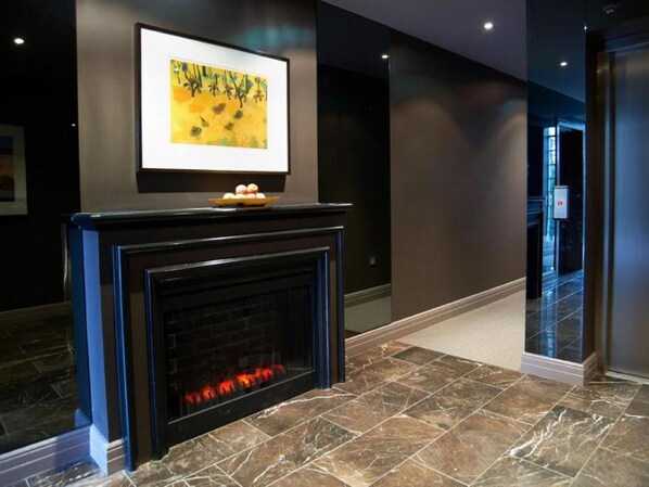 A modern lobby with a black fireplace, a framed abstract painting, and a marble floor.