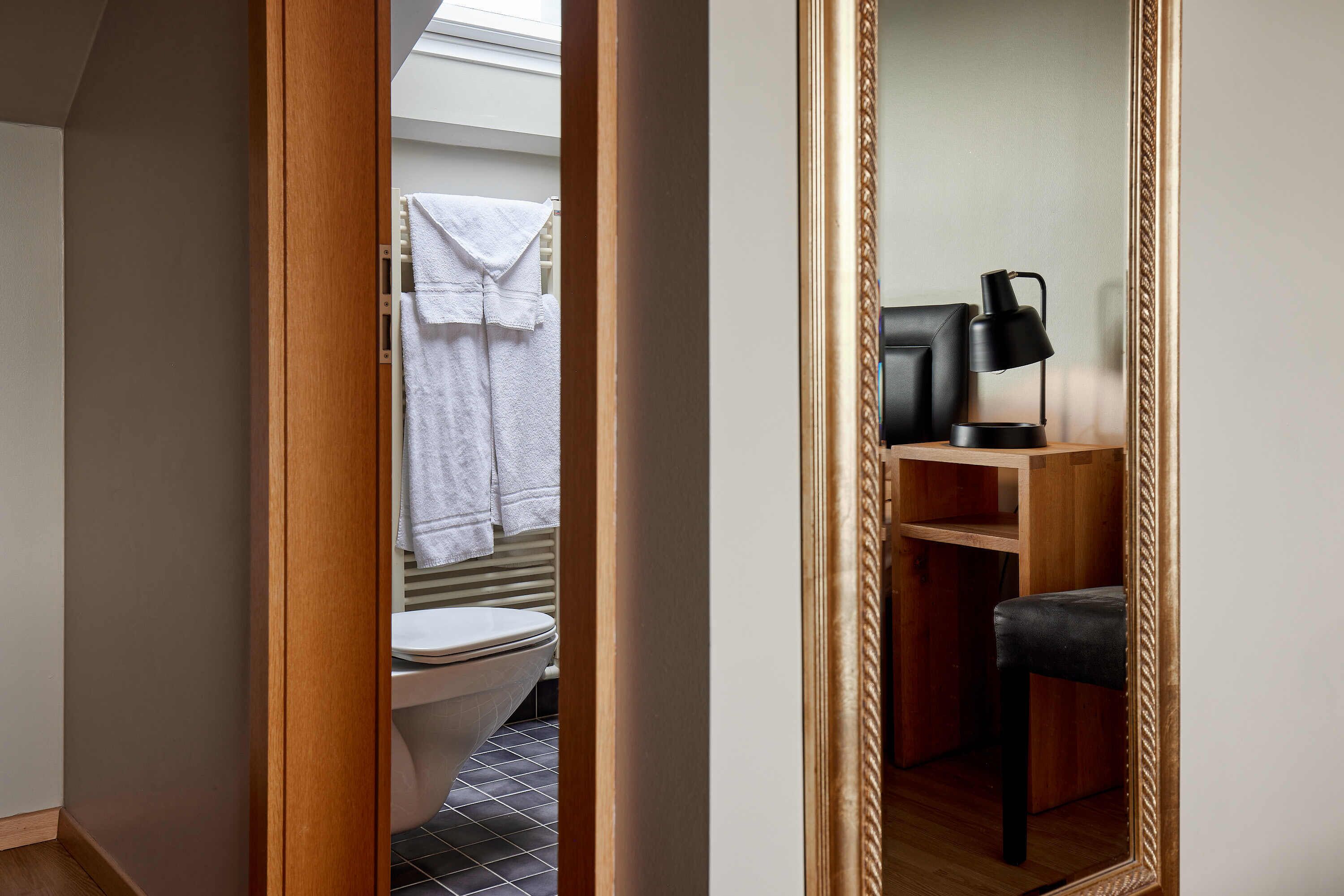 A modern bathroom with a toilet, a towel rack, and a wooden vanity with a black lamp.