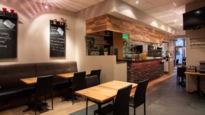 A restaurant with wooden tables and black chairs, a counter with a menu, and a television on the wall. - Hotel Fron (Reykjavik)