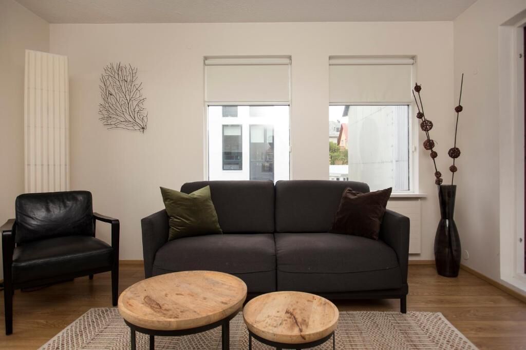 A living room with a dark grey sofa, two wooden coffee tables, a black leather chair, and a decorative wall piece.