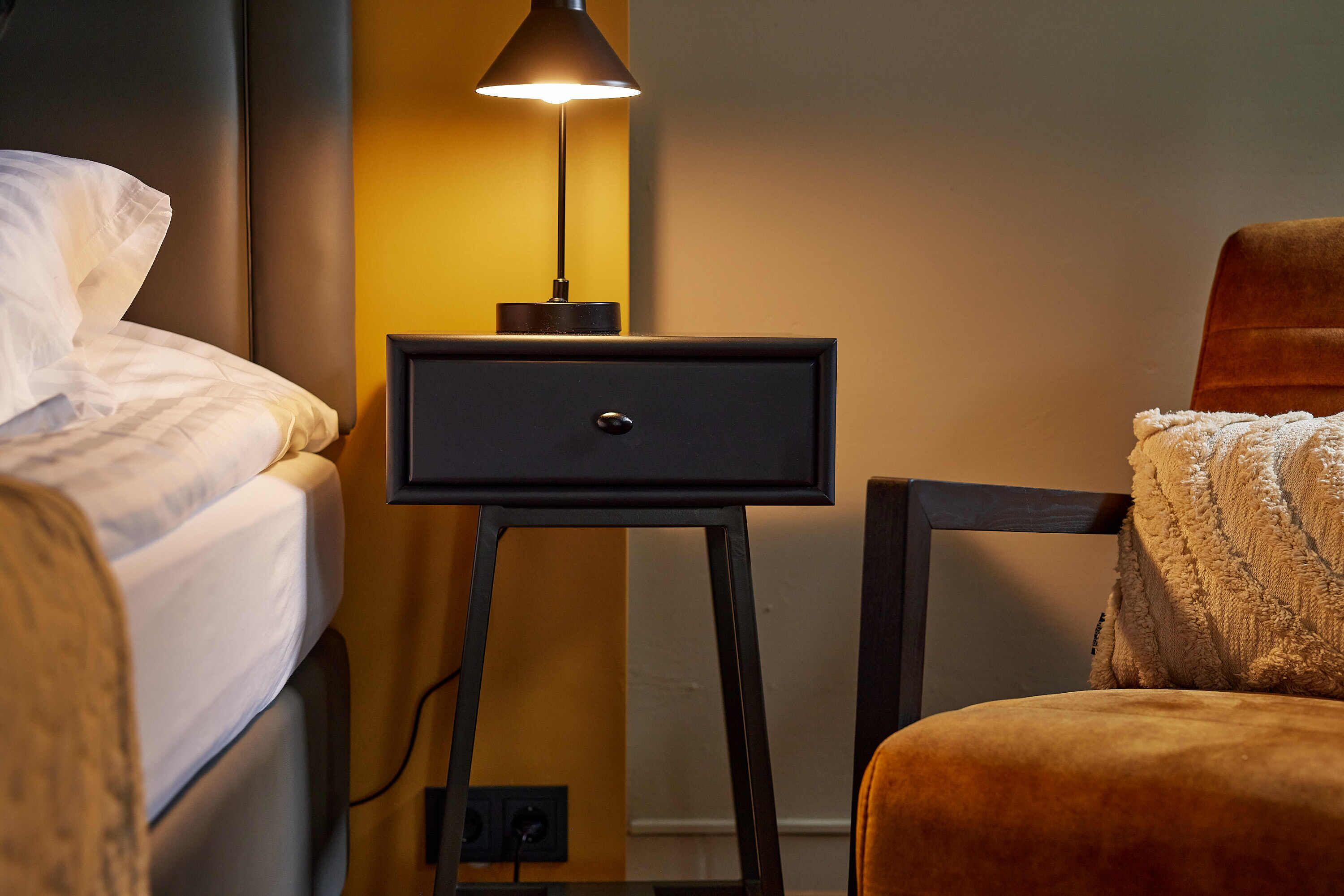Un dormitorio con una cama, una mesita de noche con lámpara y una silla.