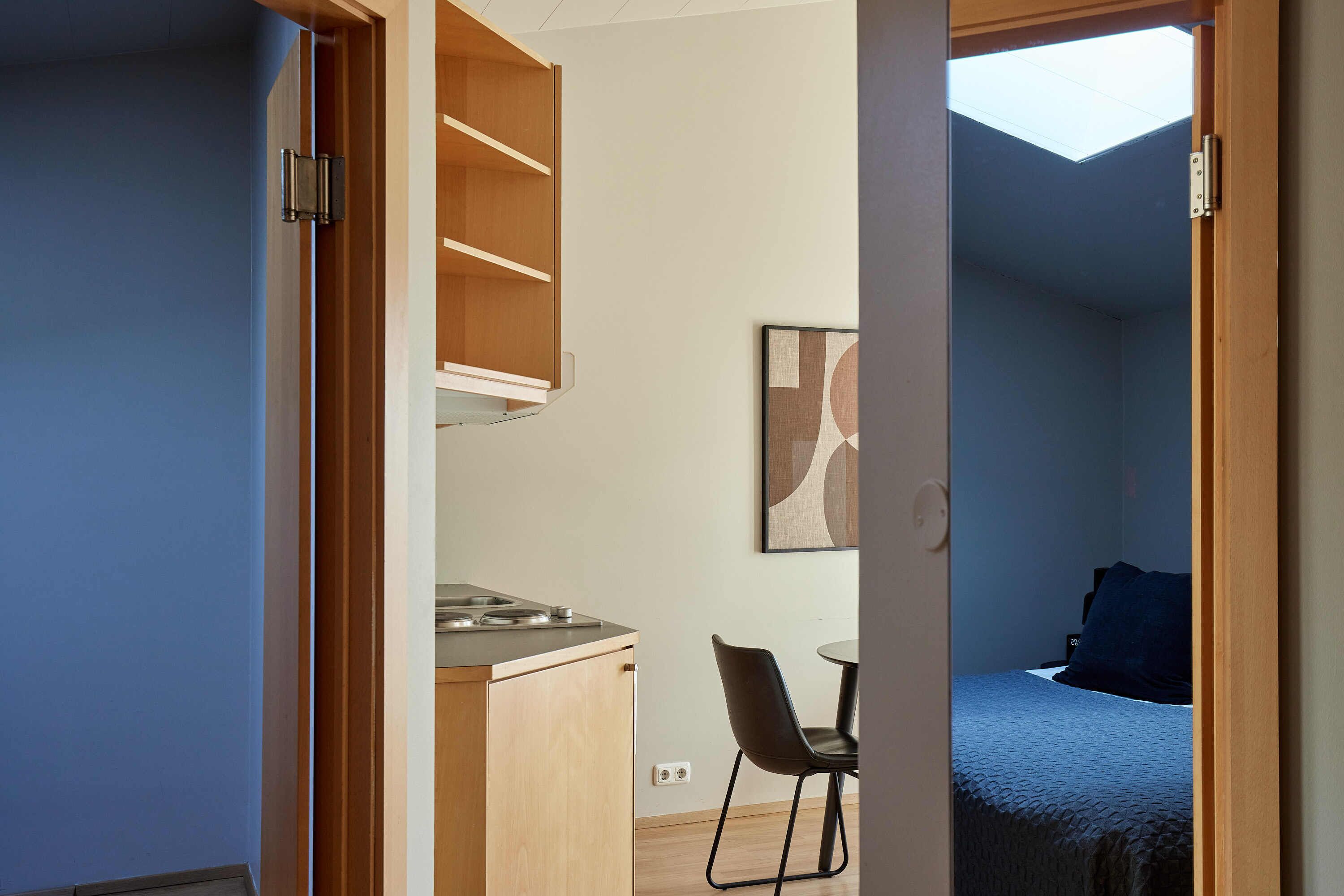 Una habitación pequeña con kitchenette, cama y una silla.