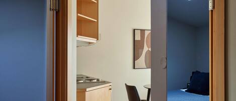 Una habitación pequeña con kitchenette, cama y una silla.