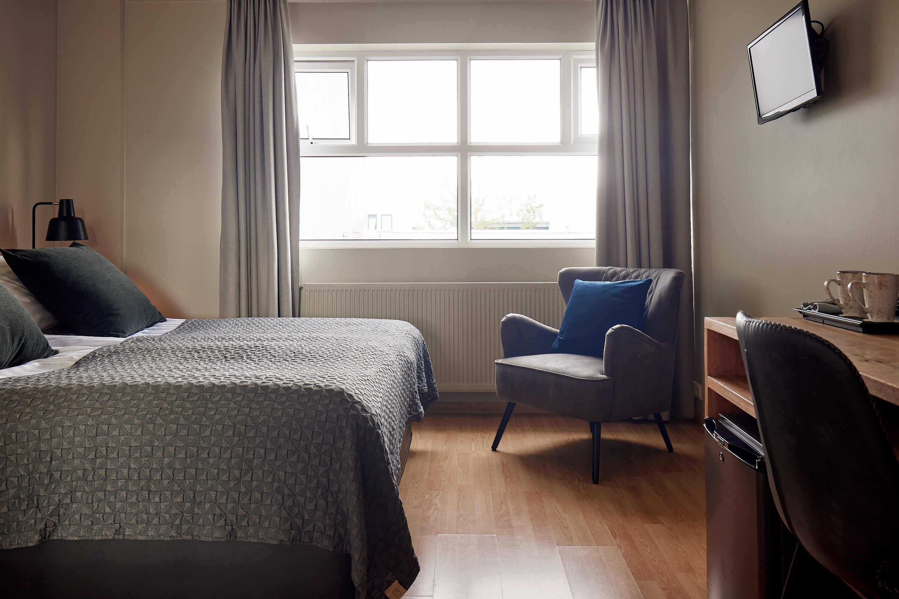 A hotel room with two beds, a desk, a chair, a TV, and a window with curtains.