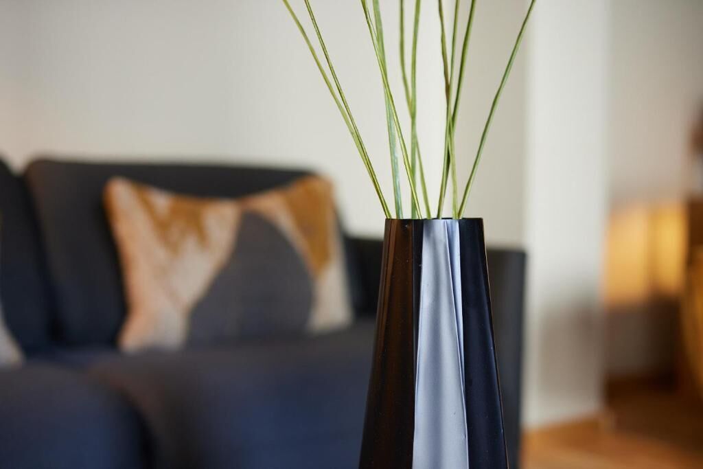 A modern living room with a dark-colored sofa and a vase with green plants.