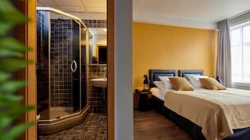 Quarto de hotel moderno com área de chuveiro, uma cama e duas almofadas, e uma mesa de cabeceira.
