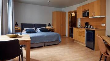 A compact bedroom with a bed, bedside tables, a desk, and a kitchenette.