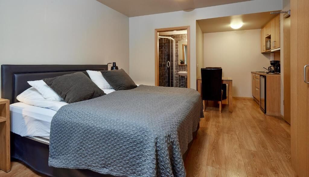 Een slaapkamer met een bed, nachtkastje en een klein kitchenette met een spoelbak en kastjes.