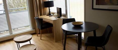 A room with a desk, two chairs, a small table, and a window with curtains.