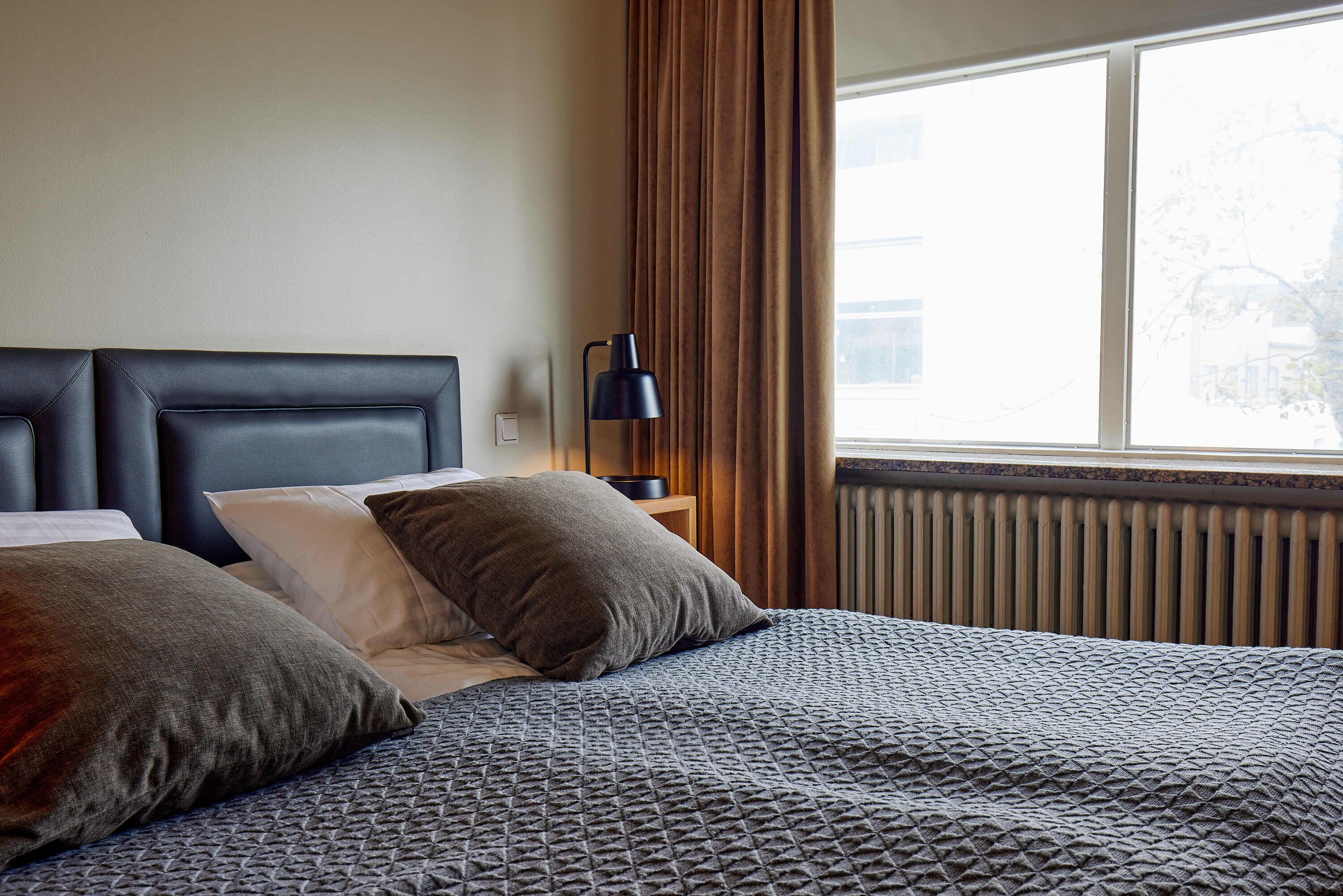 A neatly made bed with a patterned bedspread, two pillows, and a bedside lamp.