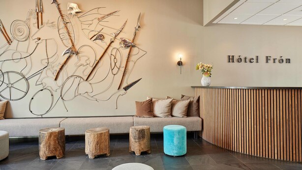 A modern hotel lobby with a reception desk, wooden stools, and a wall art installation. - Hotel Fron (Reykjavik)