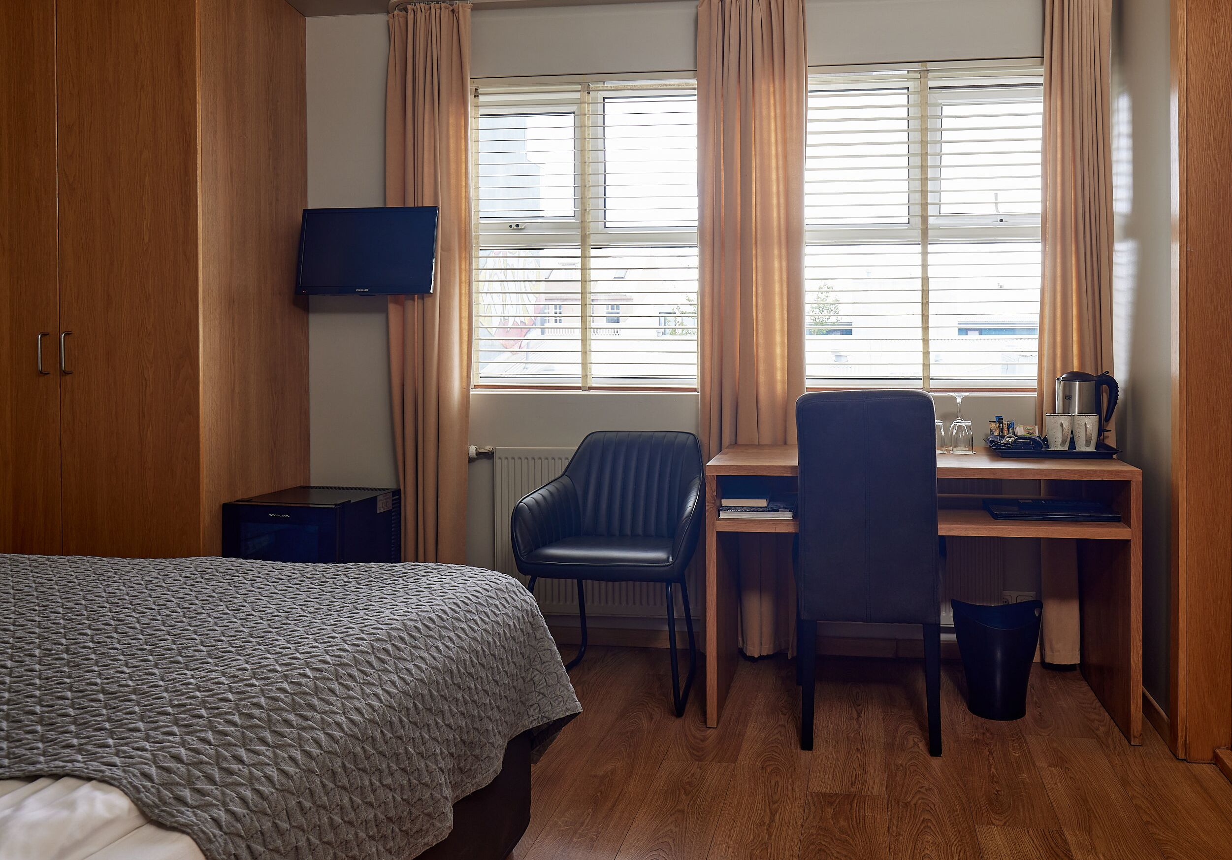 A hotel room with a bed, a desk, a chair, a TV, and a window with curtains.