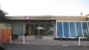 The exterior of the Cimino Hotel with a modern facade, large glass entrance, and a parking area with a patterned ground. - Ciampino Hotel (Ciampino)