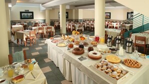 A buffet setup with various food items and beverages, arranged on a long table in a spacious dining area with multiple tables and chairs. - Ciampino Hotel (Ciampino)