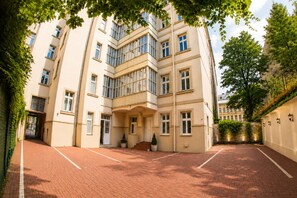 A multi-story building with a brick-paved courtyard, large windows, and a tree in the foreground. - Hotel Louis Leger - Czech Leading Hotels (Prague)