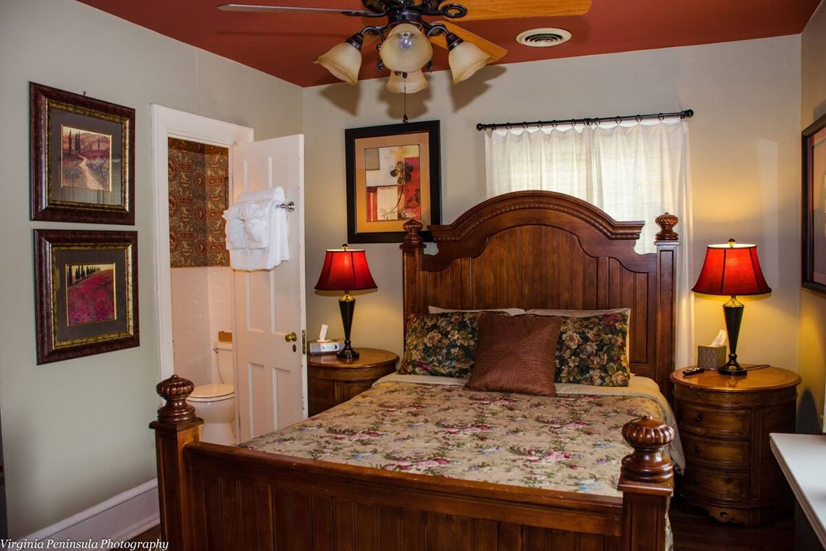 A bedroom with a wooden bed, two bedside tables with lamps, a ceiling fan, and framed artwork on the walls.