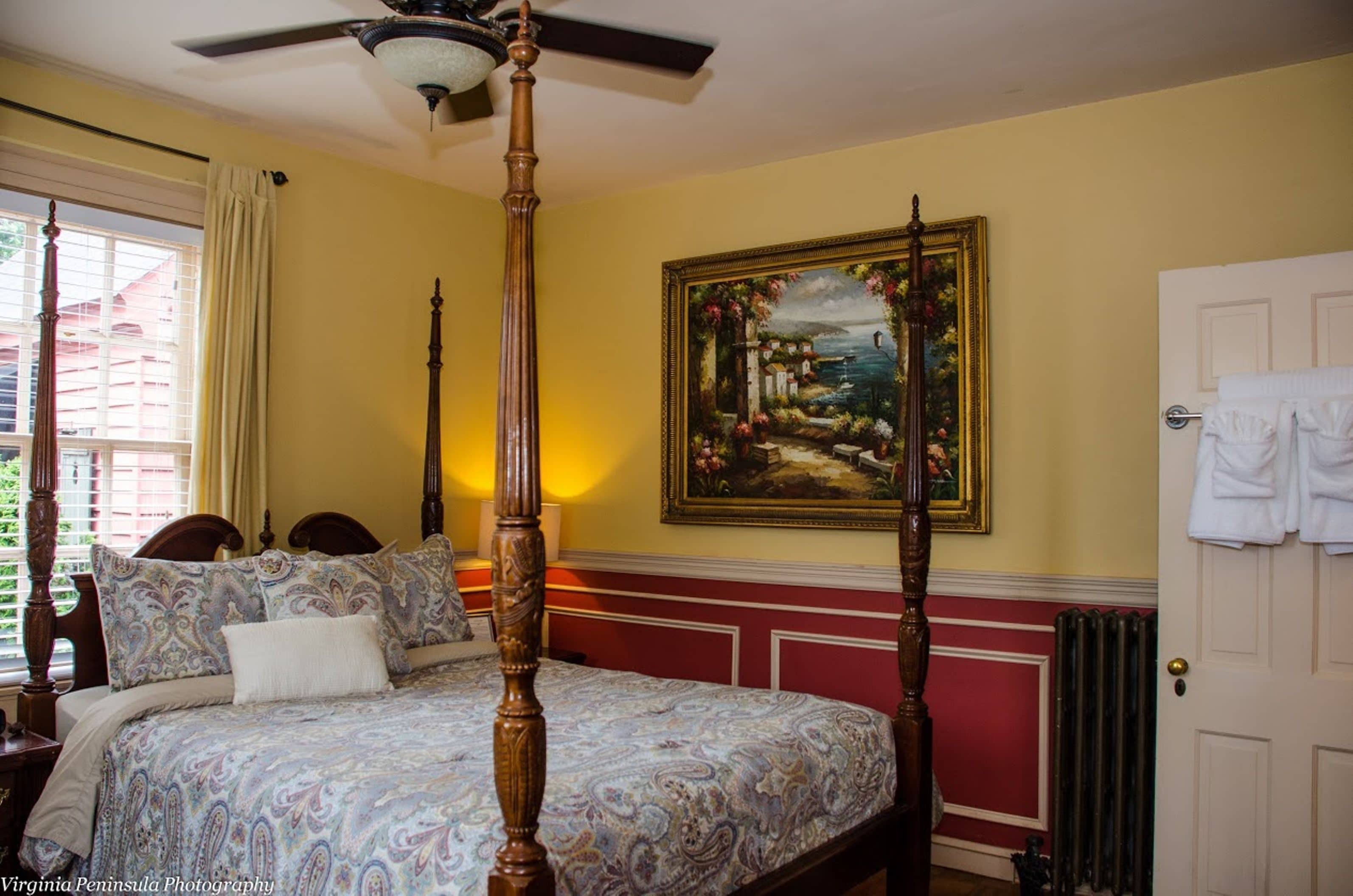 A bedroom with a four-poster bed, a painting on the wall, and a window with curtains.