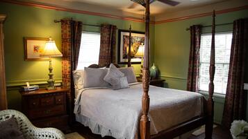 A four-poster bed with a wooden headboard, a nightstand with a lamp, and a chair with a cushion.