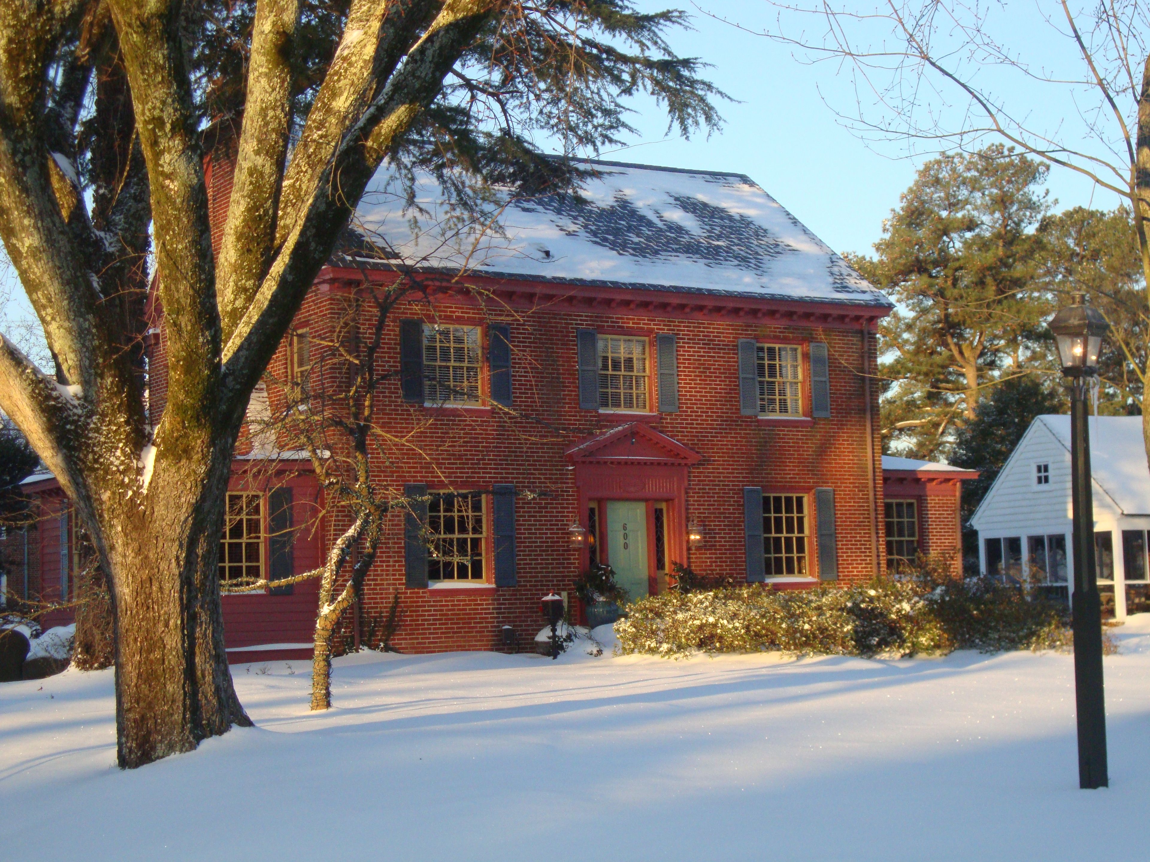 A red brick house with a snow-covered roof and a green door.