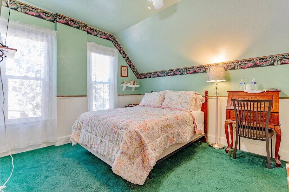 A bedroom with a bed, a chair, a nightstand, a lamp, and a window.