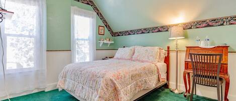 A bedroom with a bed, a chair, a nightstand, a lamp, and a window.