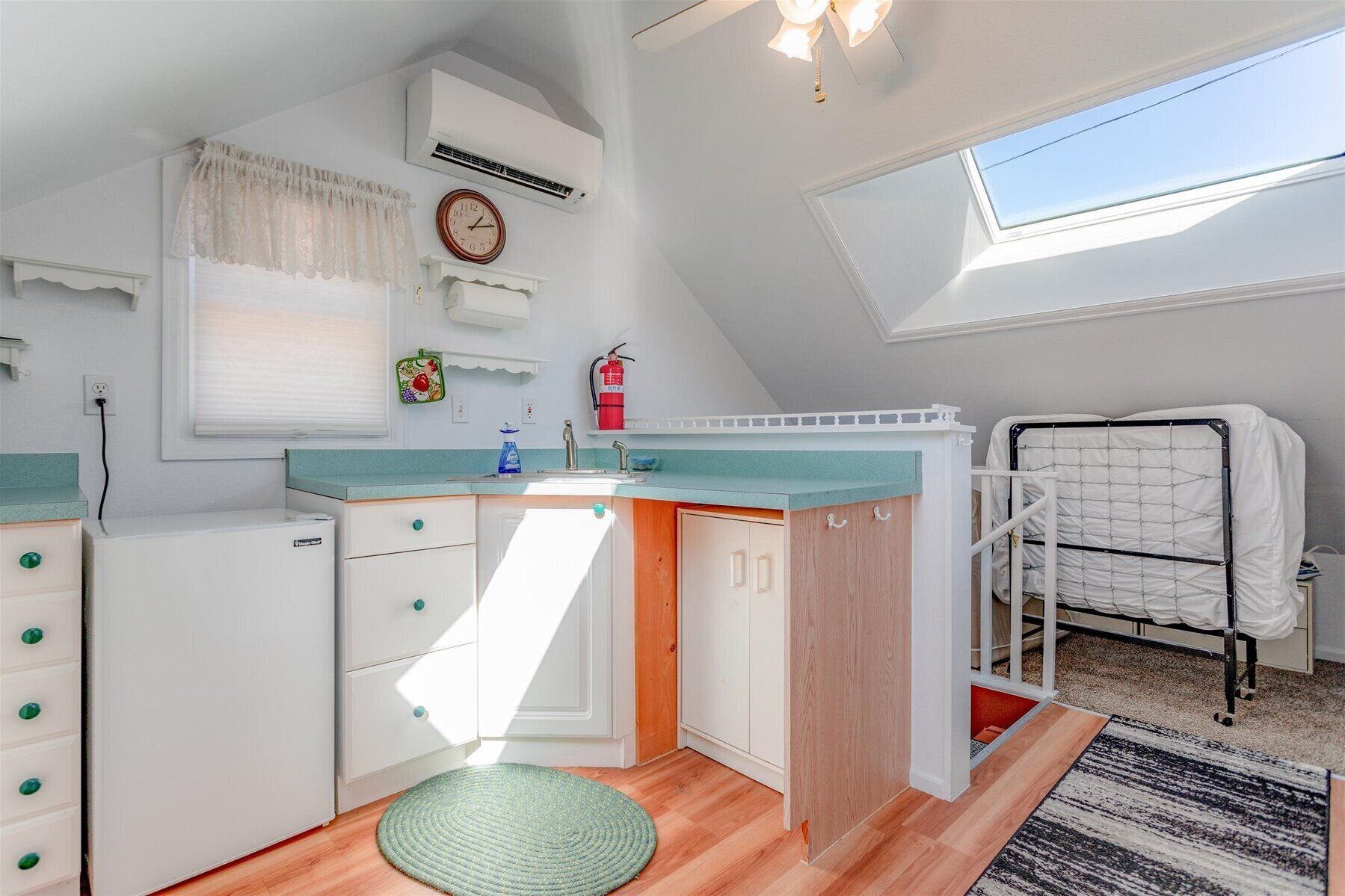 A compact, well-lit room with a kitchenette, a bed with a safety rail, a skylight, and a small window.