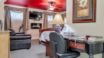 A hotel room with a bed, a desk, a chair, a ceiling fan, a TV, and a framed picture on the wall.