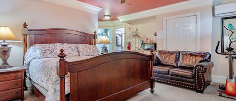 A bedroom with a wooden bed, a leather sofa, a ceiling fan, and a door.