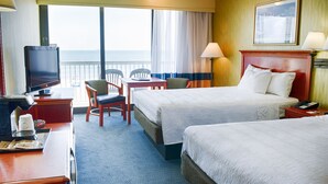 A hotel room with two beds, a desk with a television, a chair, a desk lamp, and a view of the sea. - Oceanfront Inn (Virginia Beach)