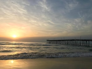 A pier extending into calm waters during sunset with a clear sky.
