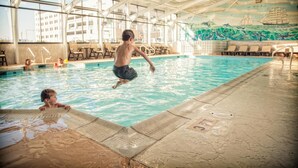 An indoor swimming pool with a mural of ships and waves on the wall, a diving board, and lounge chairs around the pool. - Oceanfront Inn (Virginia Beach)