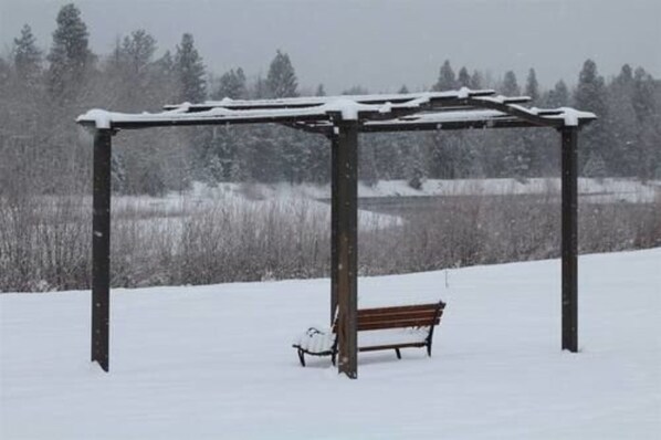 A snow-covered outdoor area with a wooden pergola and a bench.