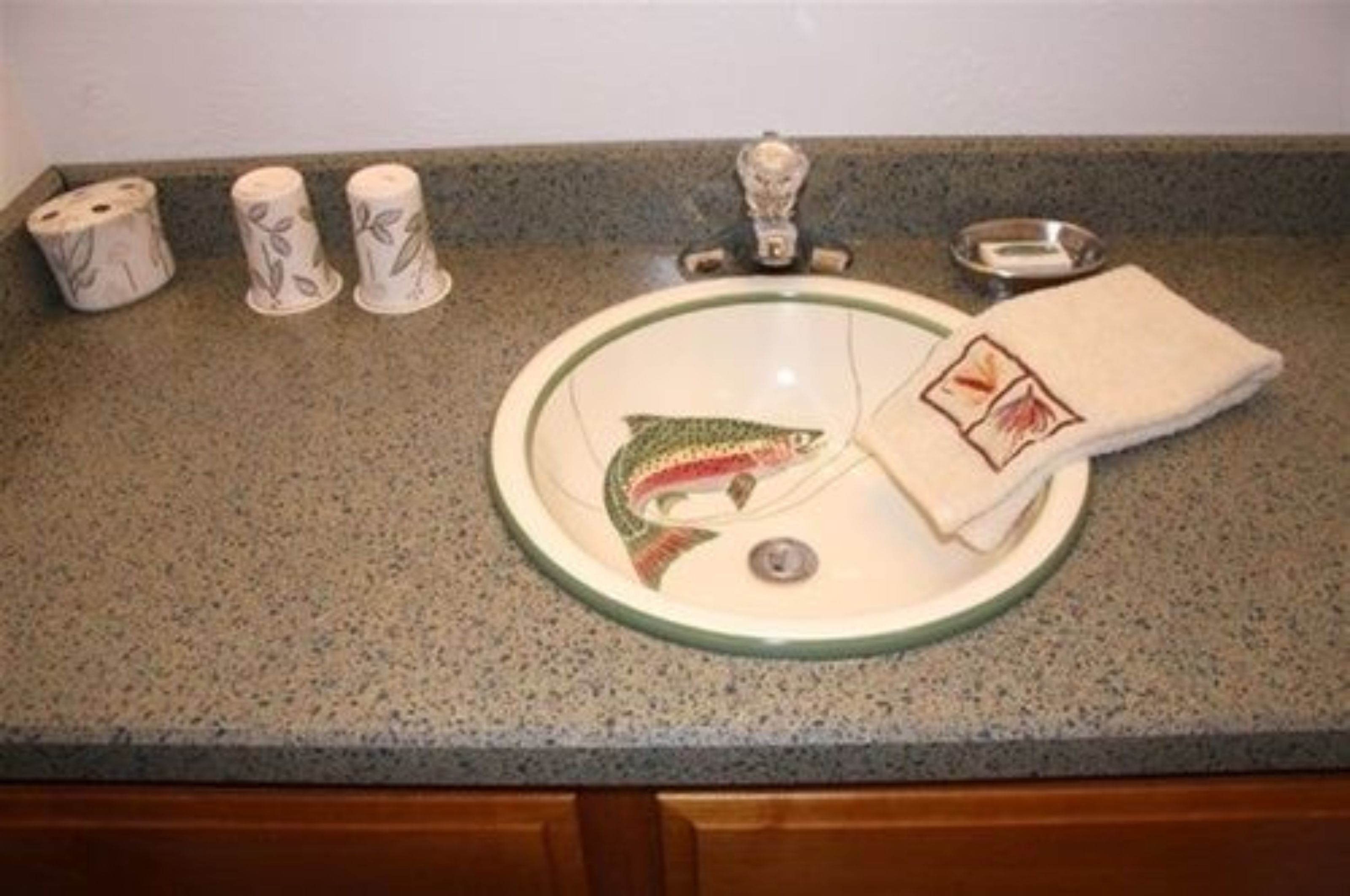 A kitchen sink with a decorative fish design, three rolls of toilet paper, and a folded towel.