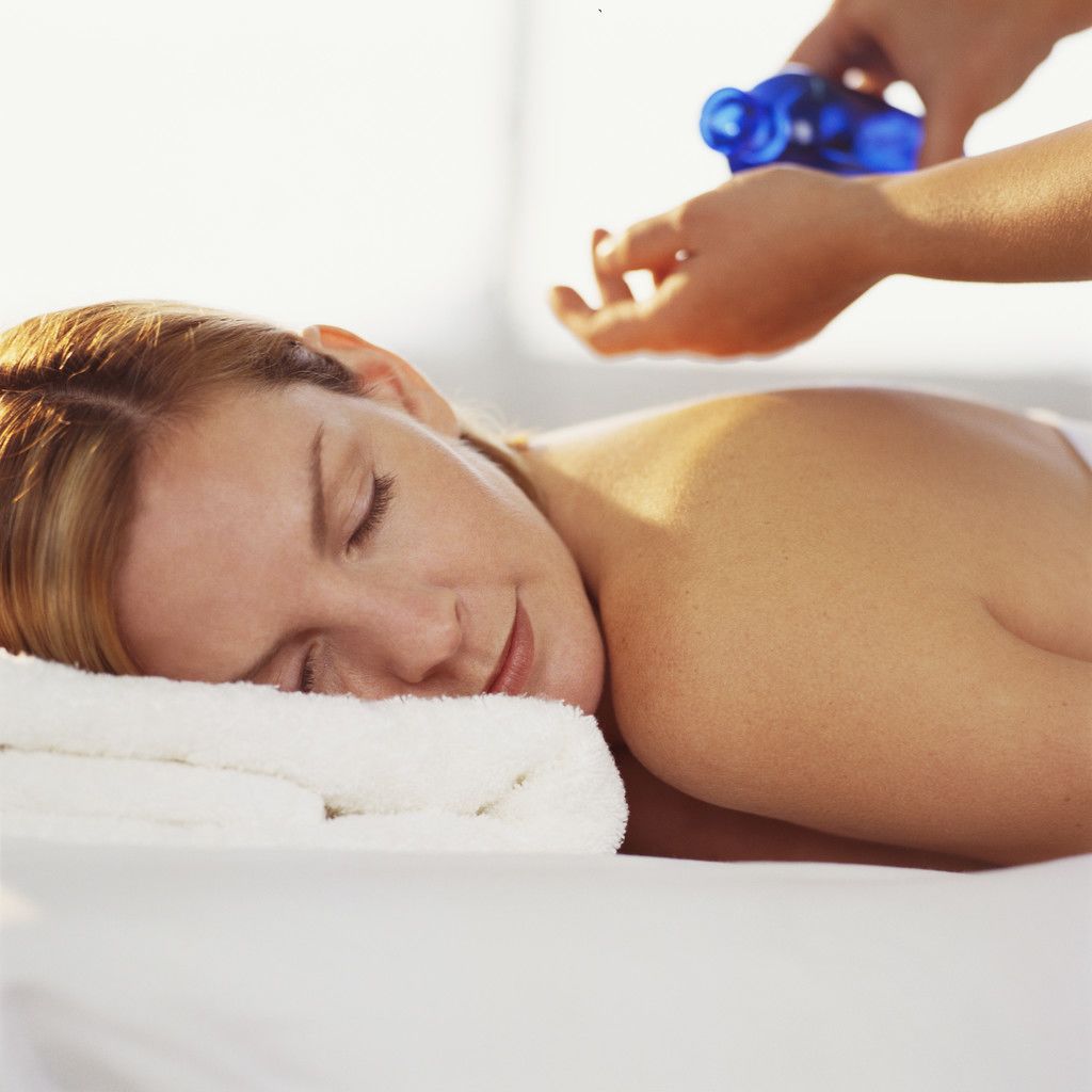 A person lying on a bed with a white towel, receiving a blue bottle treatment.
