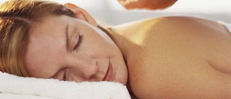 A person lying on a bed with a white towel, receiving a blue bottle treatment.