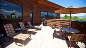 A modern outdoor seating area with wooden furniture and a large umbrella, overlooking a scenic landscape. - Carson Valley Inn (Minden)