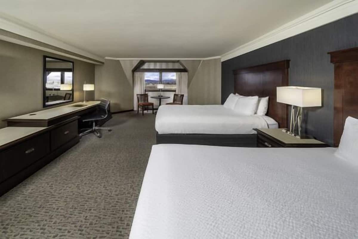 Une chambre d’hôtel avec deux lits, un bureau, une chaise et une petite table.