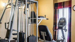 Uma academia com diversos equipamentos de exercícios, incluindo uma máquina de polia, um banco e um aparelho elíptico.