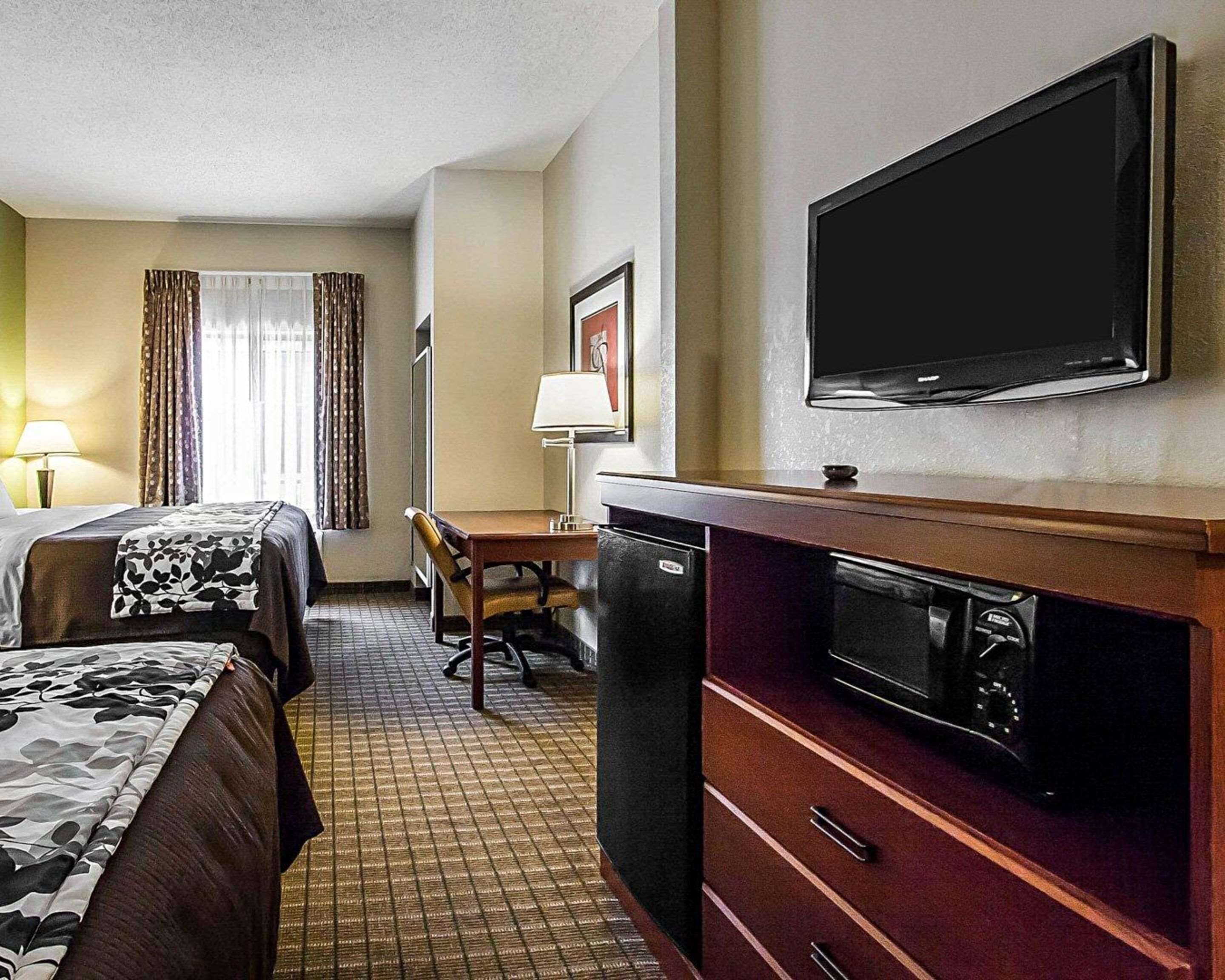 A hotel room with a bed, a desk, a chair, a television, and a microwave.